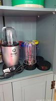 Magic Bullet blender base with two clear plastic cups and one black lid on shelf