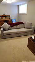 Full view of light grey sofa against wall with two seat cushions, two back cushions, two square pillows and red throw