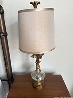 Full view of one lamp showing fabric shade, ornate metallic top finial, and mercury glass base on wooden table.