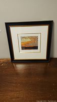 Framed numbered print of Sunset Sky by Tom Thomson on wooden surface.