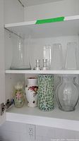 Shelves with multiple vases made of glass and ceramic, and two small silver metal candle holders