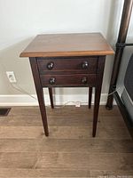Front view of the wooden bedside table showing two drawers with round knobs and slim legs.