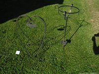 Wide shot of both metal plant stands placed on grass outdoors, showing overall size, shape and condition.