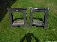 Front view of two Stanley folding sawhorses showing wear and paint stains, placed on grass.