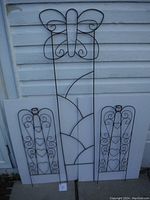 Full view of all three metal wire garden trellises against white siding, two angels with heart shapes and one butterfly design.