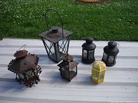 Photo of six decorative garden lanterns placed on ground; various shapes and sizes with rustic and rusty look