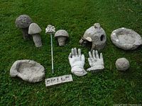 Full set of nine garden decor pieces arranged on grass, showing mushrooms, hands, birdbath, small planter, and engraved block.