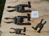 Three metal clamps of varying size and color laid on plywood outdoors, good lighting shows condition