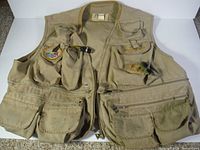 Front view of large tan Fenwick fishing vest showing numerous pockets and included fishing flies attached to the vest.
