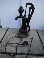 Front view of the entire cast iron water pump with attached electrical cord, placed on concrete blocks outside.