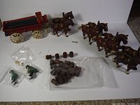 Full lot showing 4 cast iron horses, barrels, pins, and green driver figurines in plastic bags with red cast iron buggy in background.