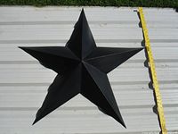 Top down view showing the full 34 inch width of the large black metal star on a white corrugated surface with a yellow measuring tape for scale.