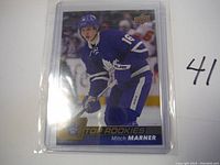 Front view of Mitch Marner rookie card in protective sleeve, showing player in Toronto Maple Leafs uniform with Top Rookies branding.