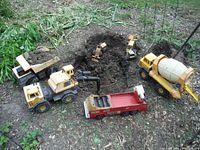 Wide arrangement of Tonka pressed steel toy construction vehicles outdoors on dirt, including dump truck, bulldozer, cement mixer, two excavators, and red truck