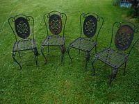 Four wrought iron chairs arranged on grass, showing overall shape and condition.