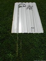 Full view of the tall thin metal shepherd's hook on grass with a white panel background.