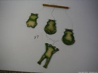 Full view of all five ceramic frog wind chimes hanging from a wooden bar, showing the sizes and arrangement.