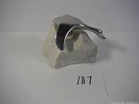 Front view of a polished metal goose sculpture mounted on a natural stone base showing the bird in a flight pose.