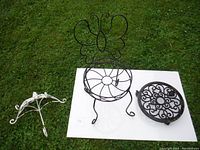 Three wrought iron plant stands and a decorative hook displayed on the ground; shows size and shape