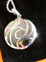 Close-up front view of round pendant showing white gold cutaway pattern over mother of pearl