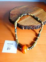 Full view of African trade bead necklace on wood background showing a large amber-colored central pendant with yellow and black patterned beads.
