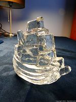 Clear thick transparent glass sailboat figurine shown on blue surface with lamp and wall background, viewed from an angled side showing layered and textured glass representing sails and water.