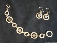 Photo of sterling silver artisan bracelet and matching earrings laid flat on white background showing circular links and dark stones.
