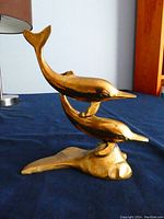 Side view of brass dolphin ornament showing two dolphins and base on dark blue fabric.