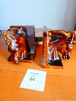 Pair of brown glazed ceramic horse head bookends, showing both pieces side by side on a wooden surface with visible nicks on the bases.