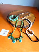 Overall view of the collection displayed on wooden slab, showing four pieces: green/white bracelet, matching necklace, black and white necklace, smaller white patterned necklace.
