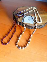 Four necklaces displayed on wooden surface including garnet cluster, carved beads, white bead and trade beads, and vintage art glass bead necklaces