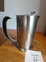Front angle view of the stainless steel coffee pot with black bakelite handle and knob, placed on a wooden surface.