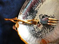 Close-up of serving fork showing copper-tone vine and leaf design on handle and silver-tone fork head with four tines.