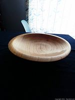 Front perspective view of hand-turned hickory wood bowl showing warm brown finish and wood grain detail on a dark surface with light curtain background