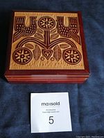 Top view of the square wooden box showing hand carved folk art floral design in reddish-brown stain/paint on natural wood background.