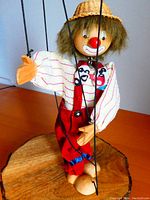 Image showing the clown marionette with striped shirt, red suspenders, straw hat, and crossed feet strings on a wooden surface.