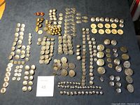 Full layout of over 200 buttons and clasps arranged on a dark cloth showing variety of shapes, sizes and metal types.