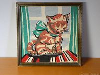 Front view of needlepoint artwork featuring a kitten with a large bow, framed in a vintage frame without glass.
