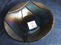 Top-down view of large fused glass bowl with blue and bronze iridescent sections and textured surface.