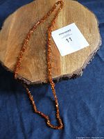 Full view of the amber chip necklace laid out on a wooden board and dark fabric, showing length and appearance.
