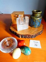 Photo showing full lot on a wood slice including the stoneware pot, the ribbed Kosta Boda candle holder, turret-shaped crystal candle holder with original box, and the three stone eggs.