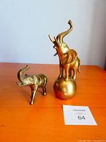 Photo showing two brass elephants, one larger standing on a ball and one smaller, both with trunks raised.