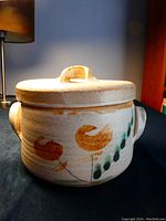 Photo of the pottery casserole dish with lid showing the exterior with stylized orange flower design and side handles.