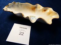 Shell-shaped dish on blue background showing overall shape and glazing details.