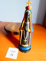 Front view of handcarved religious statue on wooden surface with auction tag visible.