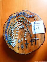 Three rosaries with varying blue and white glass beads displayed on wood slab with four small religious medallions and crucifixes