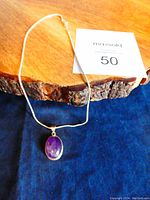 Pendant and chain laid out on wood and blue fabric for full view of necklace and pendant design.