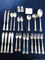 21 silver flatware pieces and pair of crystal salt and pepper shakers laid out on dark cloth