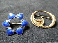 Top view of two brooches: blue enamel heart circle brooch and silver Viking ship brooch
