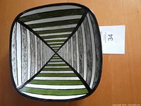 Full top view of the square ceramic plate showing handpainted geometric design in green, black, grey and white.